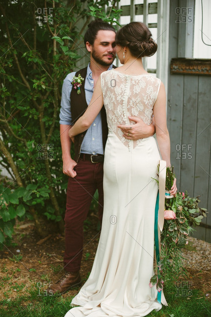 Bride and groom standing with arms around each other by a barn