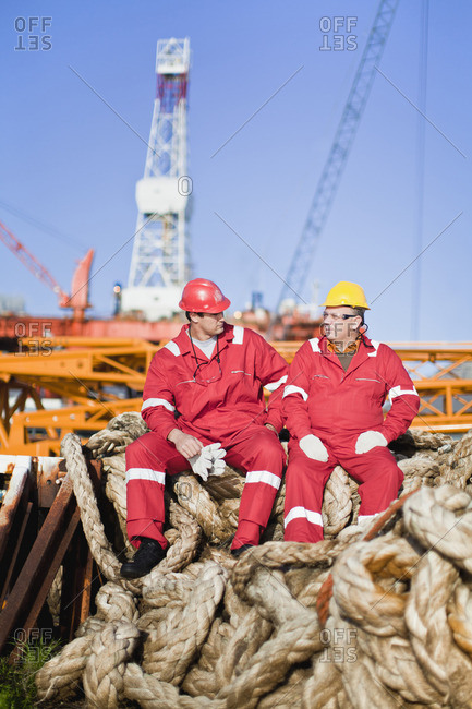 Workers sitting on rope on oil rig
