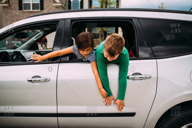 Two children hanging out window of white car