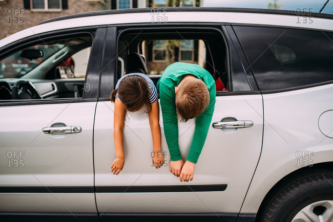 Two children hanging out the back seat window of white car