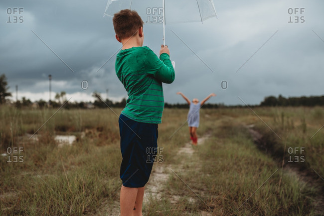 Boy standing under umbrella while his sister dances in the rain
