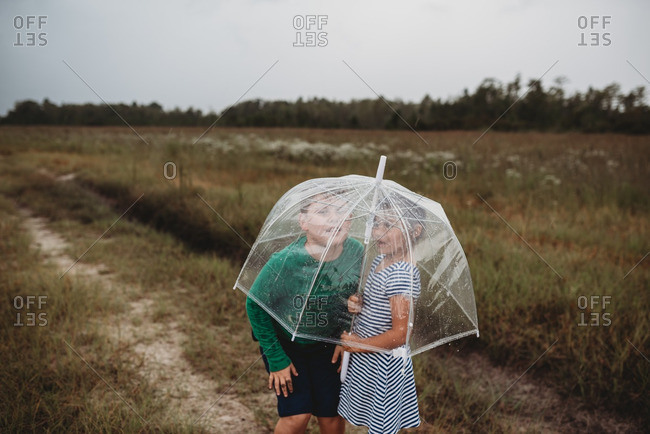 Children standing under a transparent umbrella in the rain