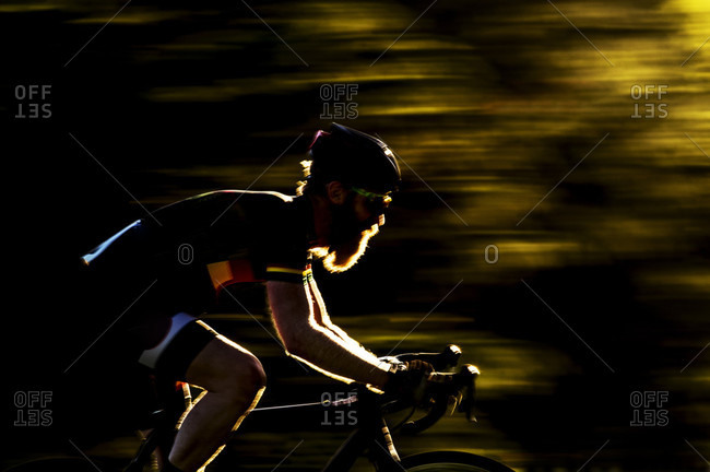 Blurred image of a bearded male cyclocross racer at speed riding through a row or trees in a race, UK