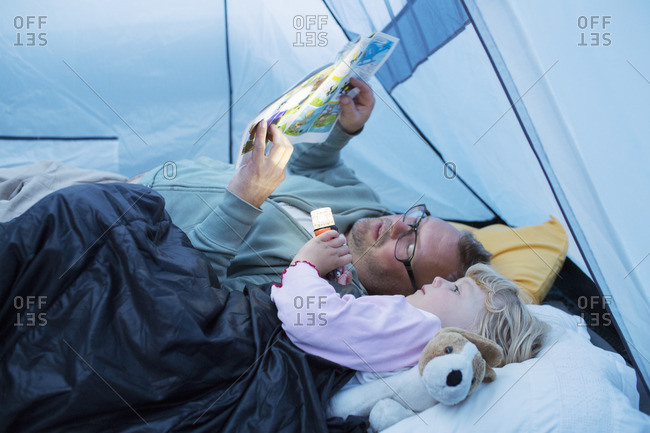 Sweden, Father and daughter reading comic book in tent