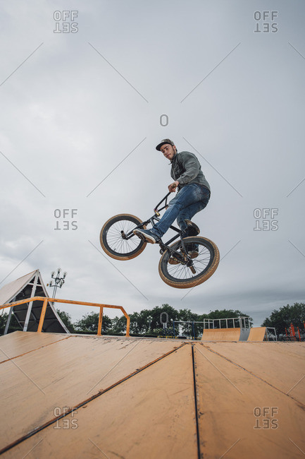Teenager performing stunt on bicycle at skateboard park against sky