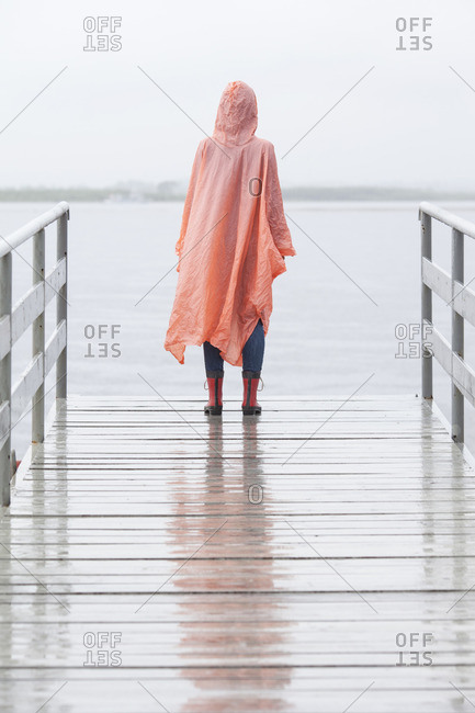 Rear view of woman wearing raincoat standing on jetty during rainy season