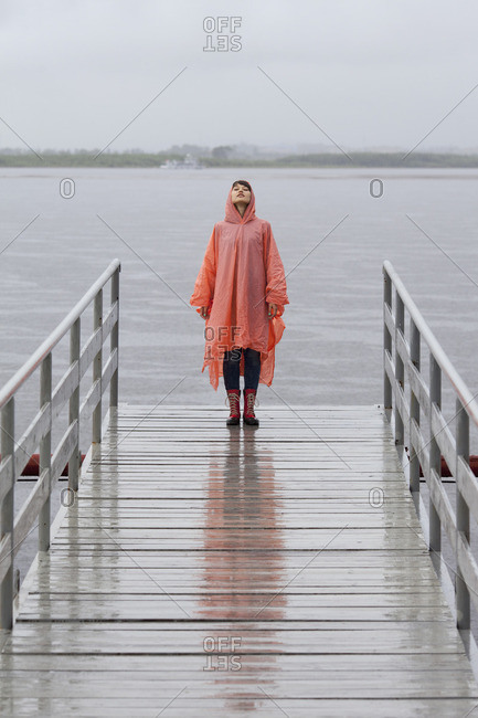 Woman wearing raincoat standing on jetty during rainy season