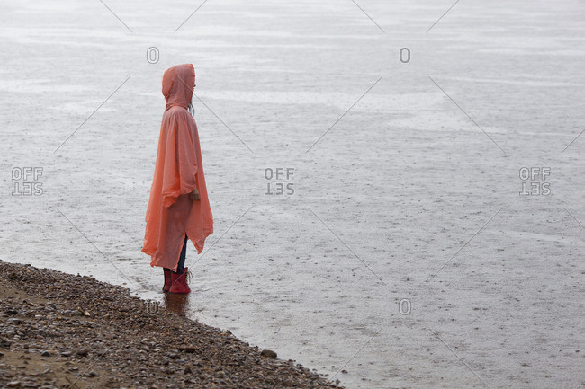 Woman wearing raincoat standing at lakeshore during rainy season