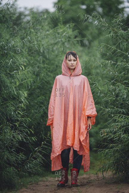 Portrait of woman wearing raincoat standing amidst plants during rainy season