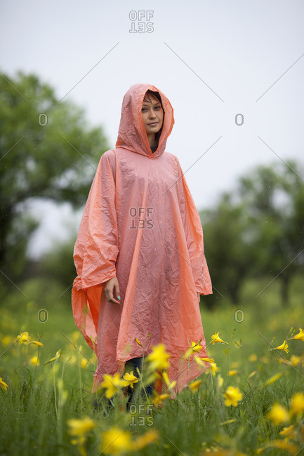 Woman wearing raincoat standing amidst yellow flowering plants in rainy season