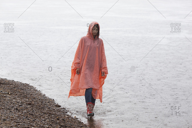 Woman wearing raincoat walking at lakeshore in rainy season