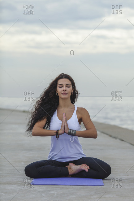 Woman with closed eyes practicing yoga in prayer position at beach against cloudy sky