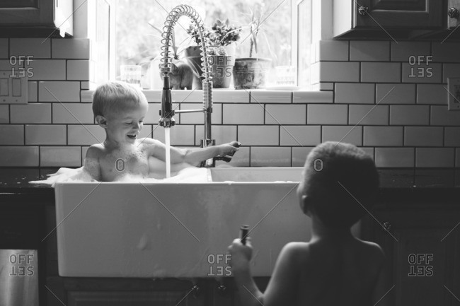 Young boy watches his brother taking a bath in a sink