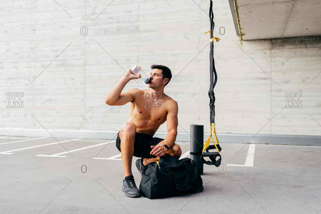 Relaxed Sportsman With Naked Muscular Torso Crouching On Street And