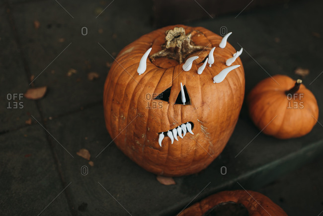 close up of spooky carved pumpkin with teeth sitting on porch