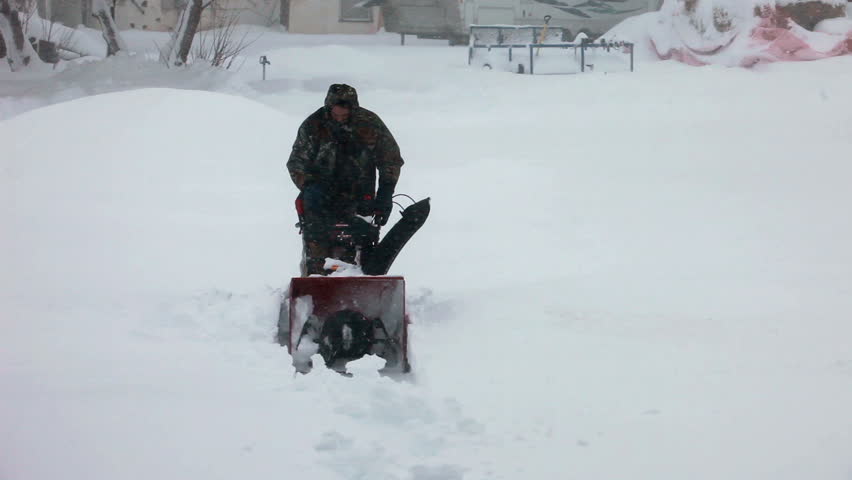 Man pushing snow blower in deep snow blizzard. Snow blowing in strong wind in sub freezing weather. Winter time hazard and climate nature.