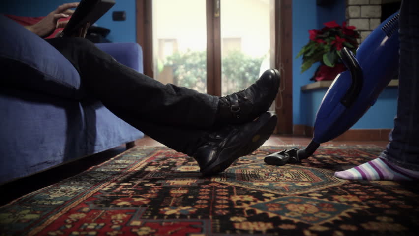 woman using vacuum cleaner on carpet and lazy man on sofa with tablet pc. Low angle view