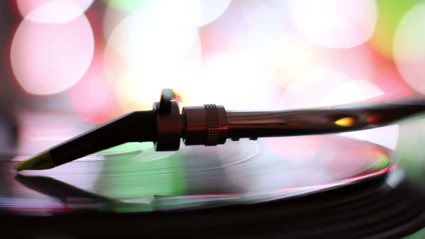close-up of the needle of dj record player, with abstract colored lights in background