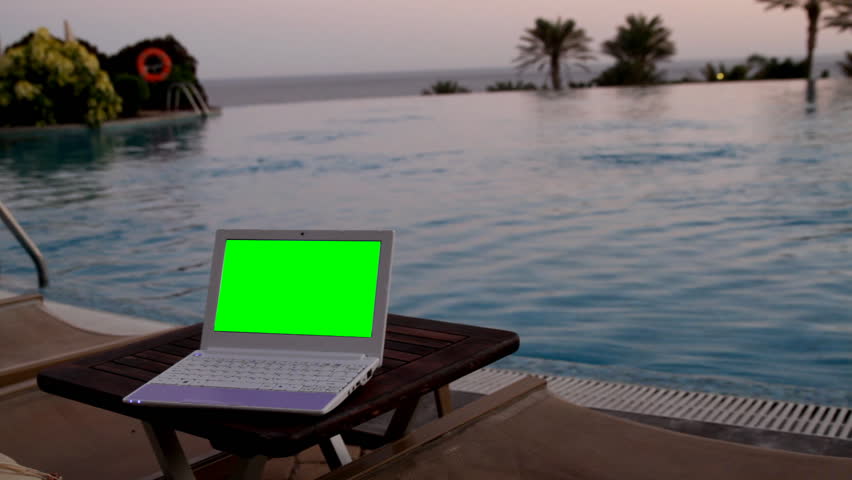 Netbook with green screen near to swimming pool in the evening 