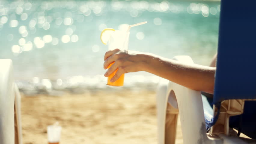 Woman lying on the sunbed and drinking exotic drink by the sea