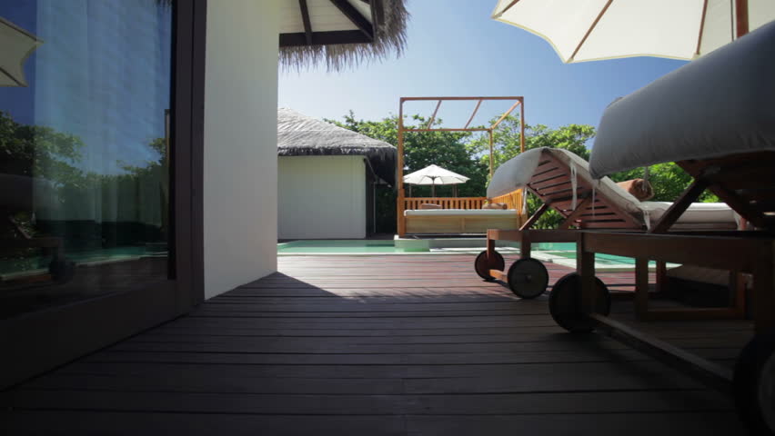 crane shot of a bungalow with sunshades and sunloungers on a tropical terrace with beach view 