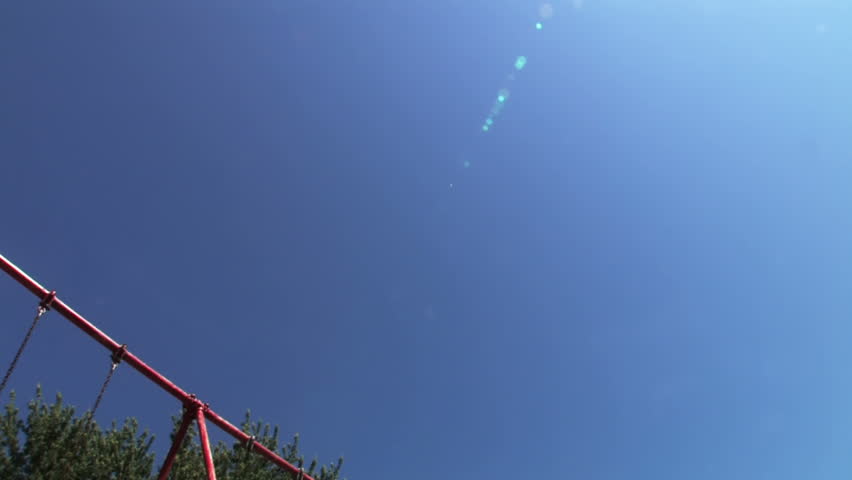 A young girl swings on a swing set in a playground  Low angle with the sky shown prominently.