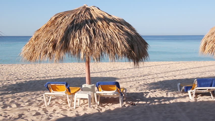 Beach scene. Nice beach view with calm Caribbean ocean, sandy beach, and deck chairs under an umbrella with woven palm leaves. Dominican Republic. 