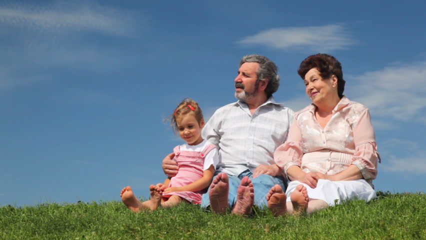happy mature couple and little granddaughter wiggling their bare feet on grass 