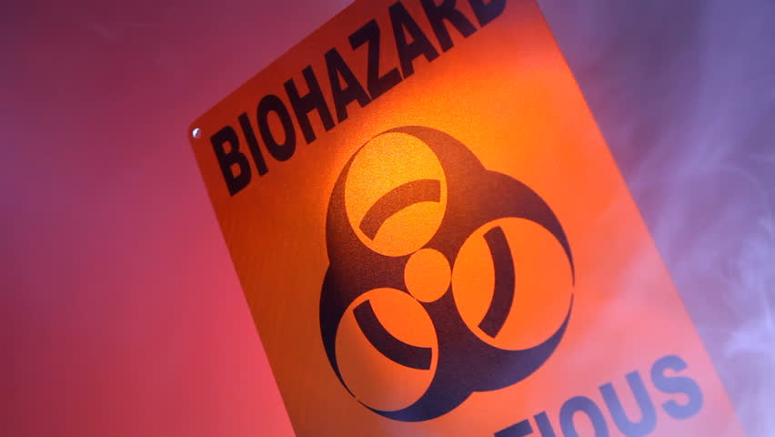 A close up of a biohazard warning sign with smoke coming into and out of the frame, and flashing warning lights reflected on the sign