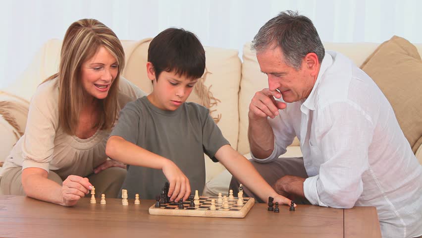 Little boy playing chess with his grandfather in the living room