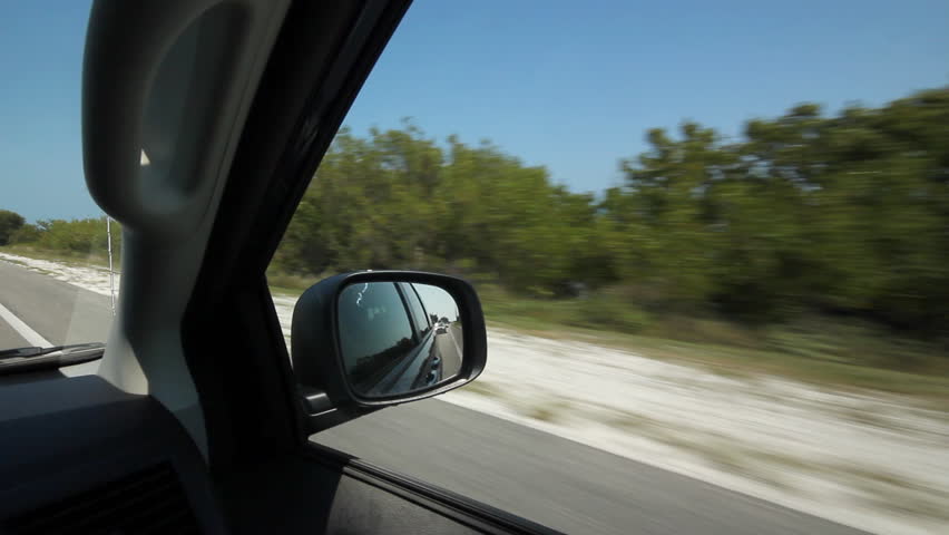 Driving in Florida Keys. Ocean view. Driving on a highway in the Florida Keys. Blue and turquoise ocean appearing through vegetation at side of the road. 
