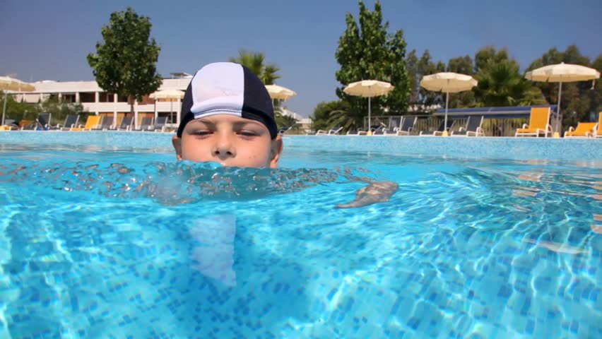 Boy in swimming cap in the pool water, the camera goes under water, and shows how he floats 