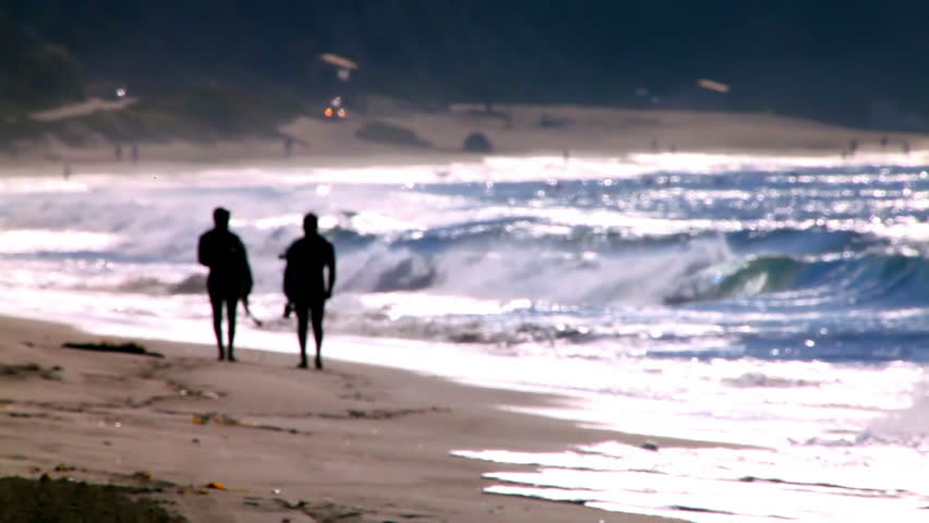 An out of focus shot of two surfers walking on a beach.
