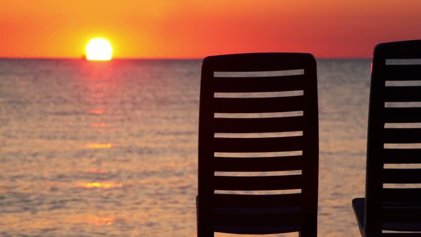 Seascape at evening sunset shown behind two deckchairs, ship on horizon shown very blured