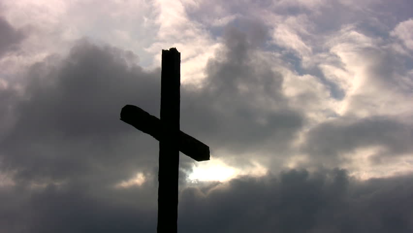 A large cross silhouetted against storm clouds at sunset.