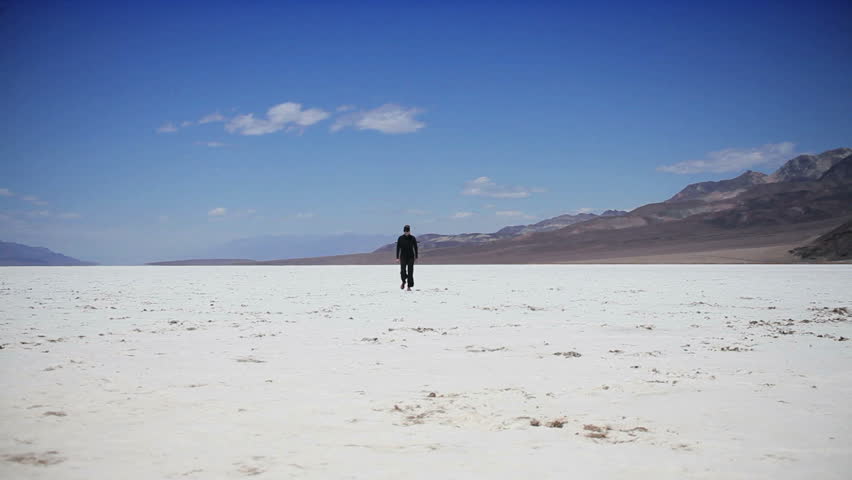 Lone figure crossing the barren environmental landscape of a dry salt lake