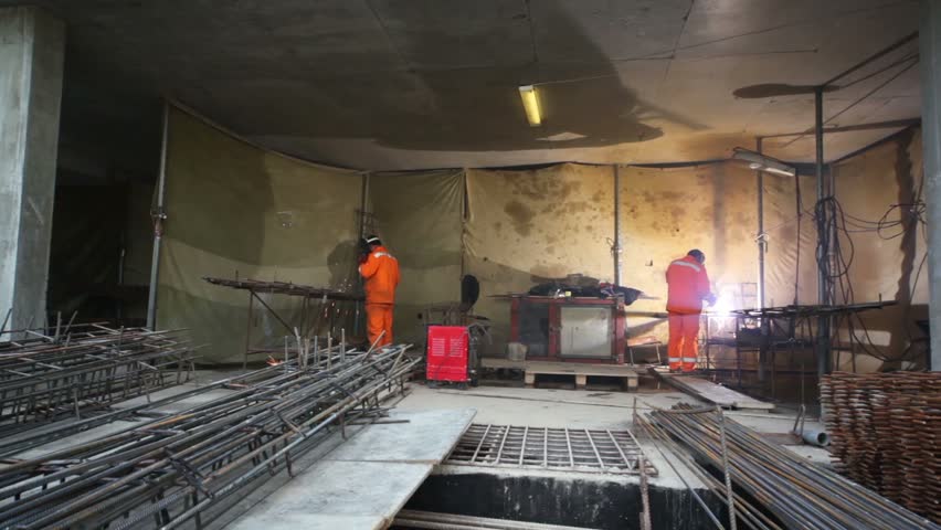 Two labourer in orange uniform weld metal gratings by acetylene torches, closer view