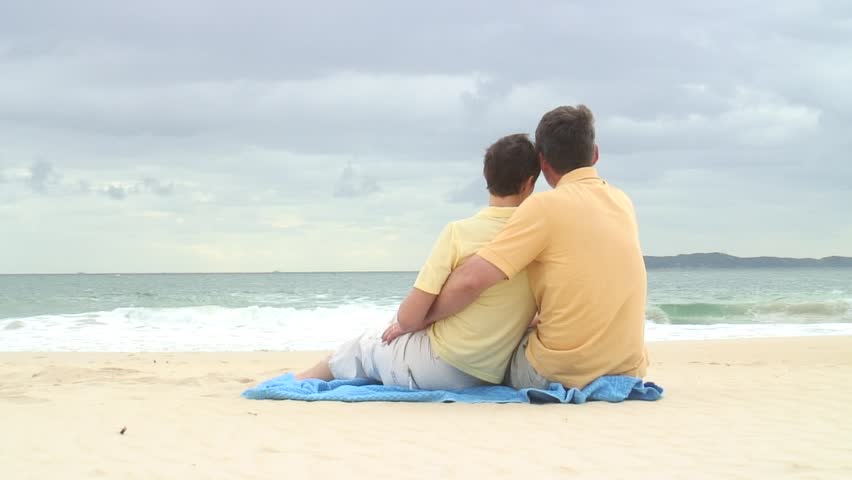HD 1080i: Couple sitting on a blue towel on the beach. Tripod.