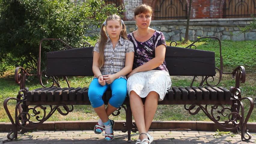 happy mother hugs her daughter sitting on beautiful bench in city by day
