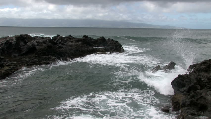 Rocky cove and bay shoreline on the island of Maui in Hawaii.  Rough surf splashing against rocks. Scenic, relaxing and calm, beautiful tropical video. Island of Molokai in distance.