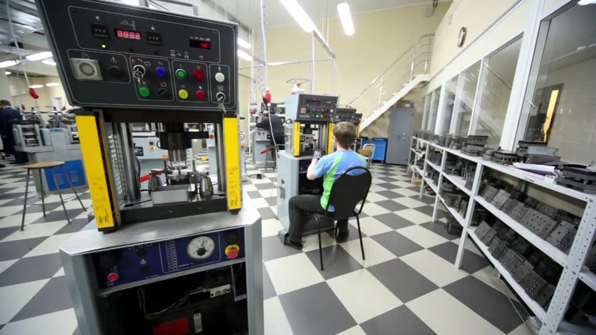 Worker stamps details on electro-mechanical press, few labourers work around