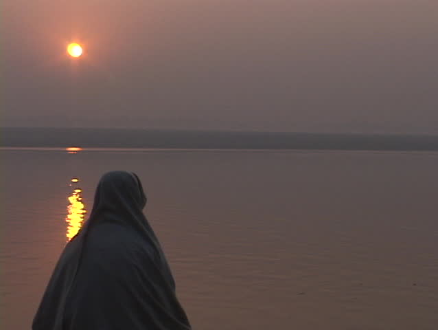 With a low sun in the distance, a pilgrim prays near the Ganges River, India.