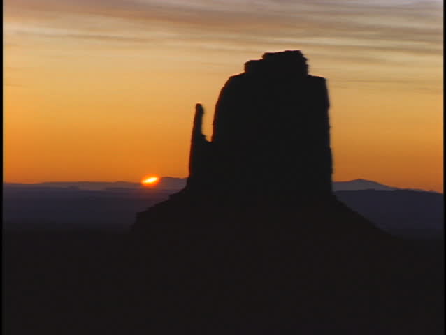 A geologic formation stands in silhouette above the horizon.
