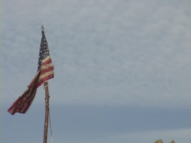 Zoom out from a flag planted in a pile of rubble left from Hurricane Katrina.