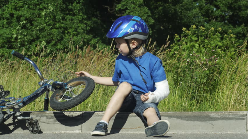 Boy with broken sitting on sidewalk.