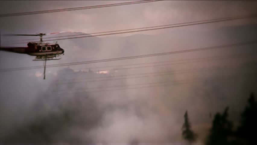 Helicopter drops water on brush fire, firemen walking along road