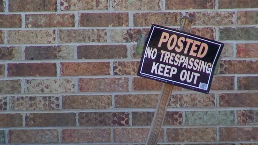 Crooked "No Trespassing" sign against brick wall
