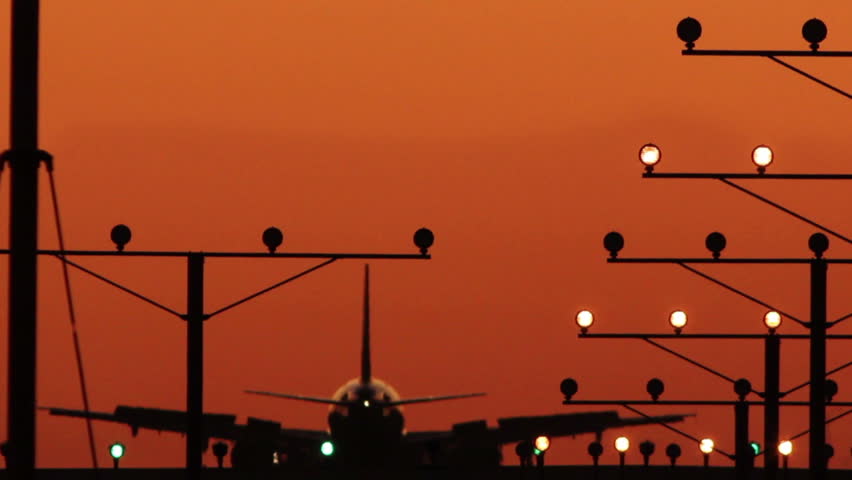 HD footage of a twin engine jet plane landing in silhouette against an orange sunset sky, followed by a defocus / camera blur out.  Jet engine audio included.