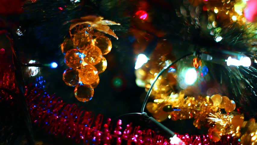 toy in form of glass grapes hanging on Christmas tree among glowing garlands, close-up