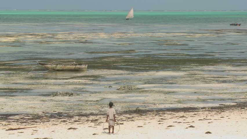 TANZANIA - CIRCA 2009: A girl stands with a toy ring on the beach gazing out at a distant sailboat circa 2009 in Tanzania.